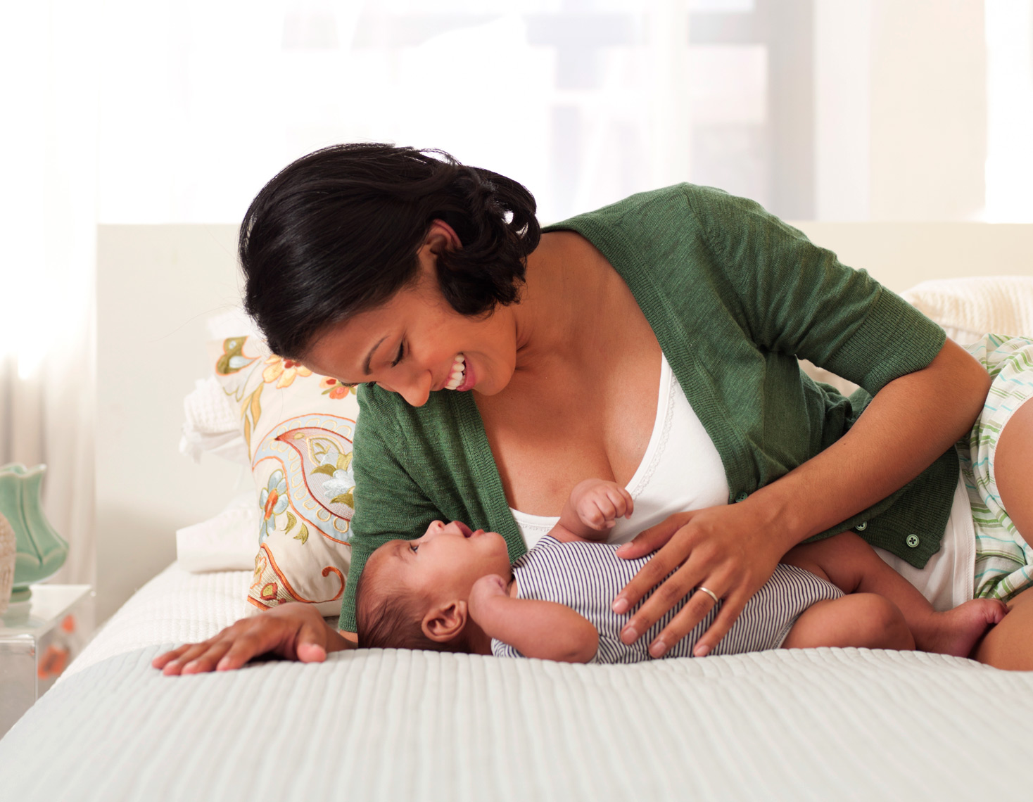 African-American mom with newborn laying on bed breast feeding