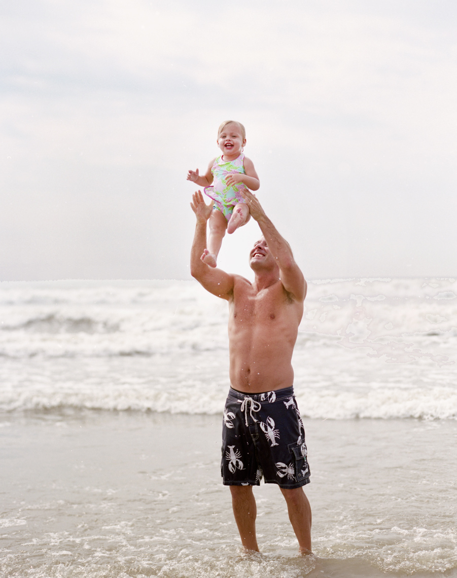man with daughter throwing her in the air on the beach