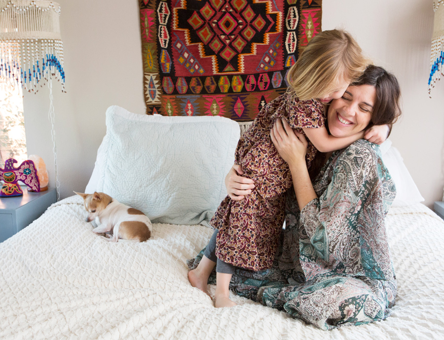 Little girl and Mom hugging while on the bed in vintage clothes by lifestyle photographer Buff Sstrickland