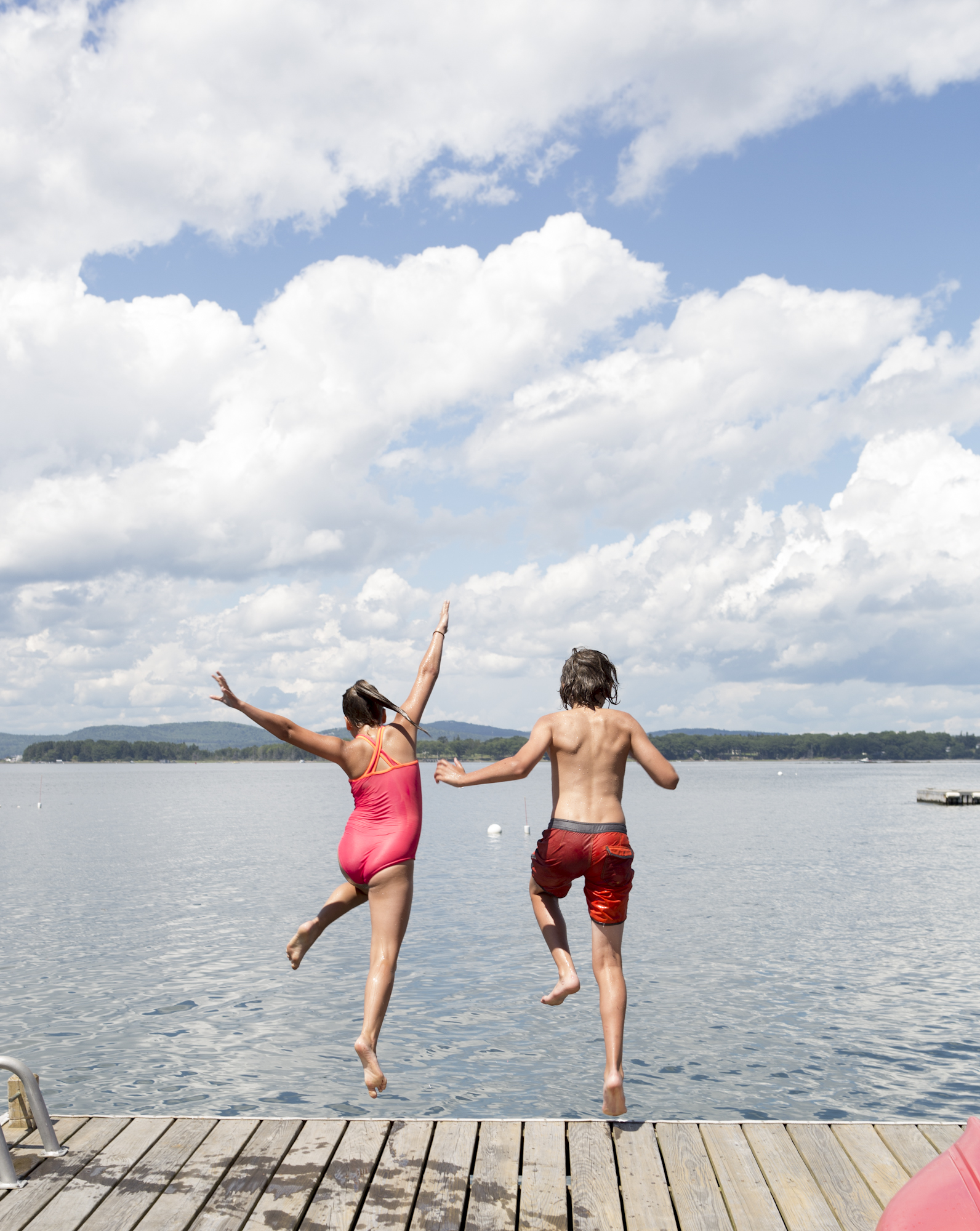 Kids jumping off a dock in summer on an island in Isleboro, Maine with brightly colored swimsuits