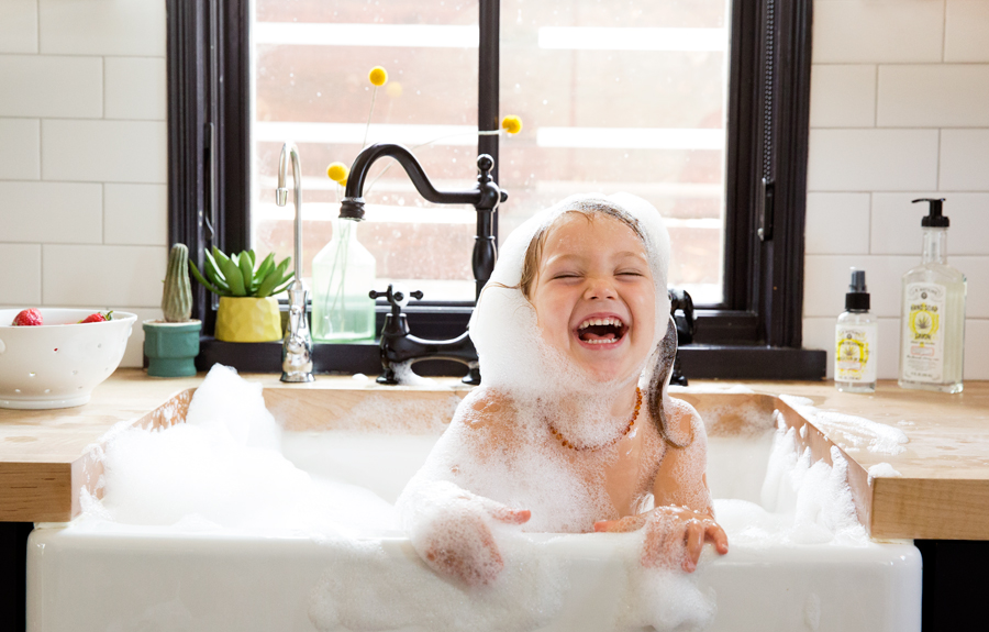 Girl having bath in kitchen sink with bubbles