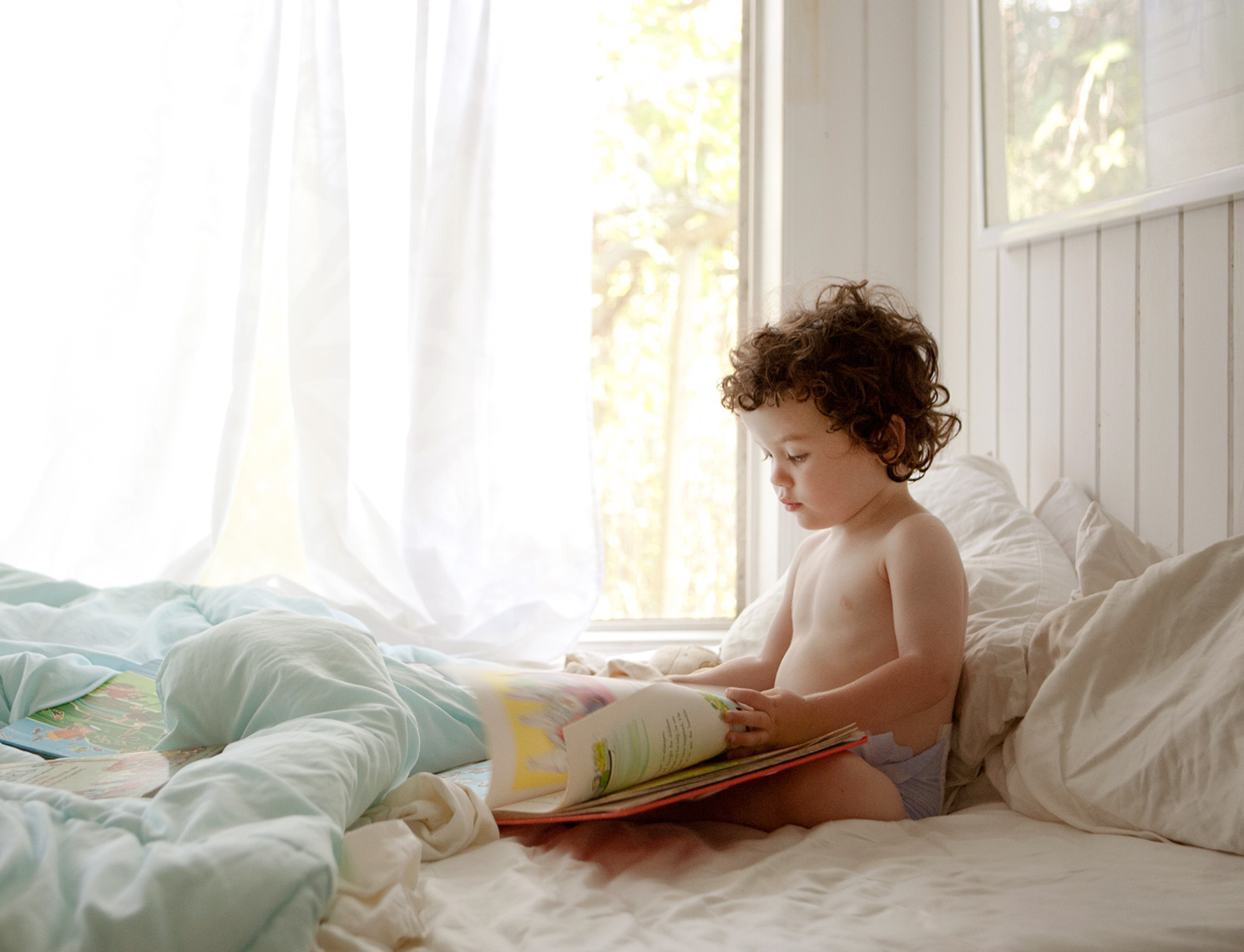 Toddler in diaper reading in bed